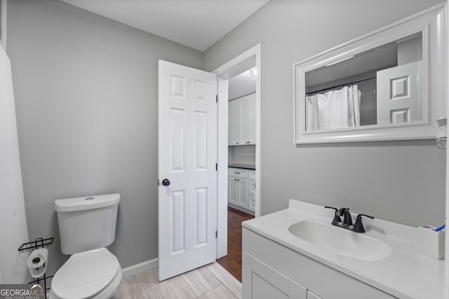 bathroom featuring decorative backsplash, baseboards, vanity, and toilet