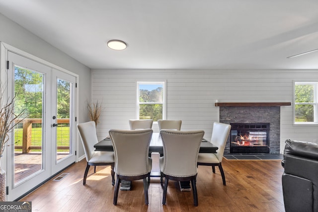 dining area featuring french doors, visible vents, a stone fireplace, and wood finished floors