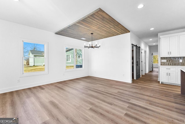 interior space featuring a barn door, baseboards, an inviting chandelier, light wood-style floors, and recessed lighting