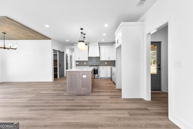 kitchen with a barn door, visible vents, backsplash, stainless steel range, and custom range hood