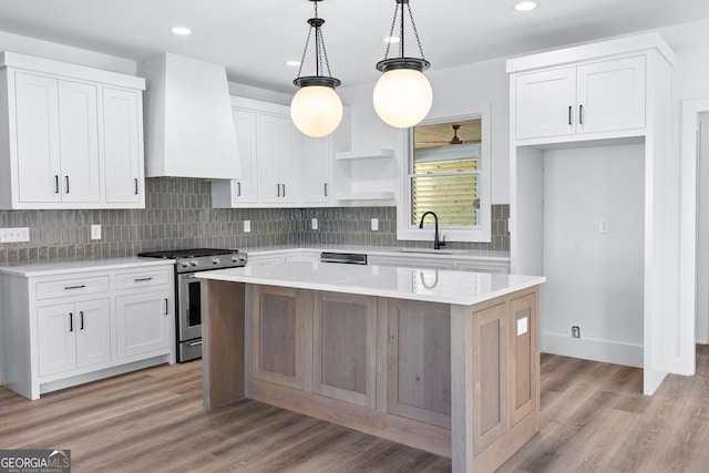 kitchen featuring wall chimney exhaust hood, a center island, light countertops, a sink, and gas stove