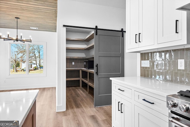 kitchen with tasteful backsplash, light countertops, a barn door, a chandelier, and light wood-type flooring