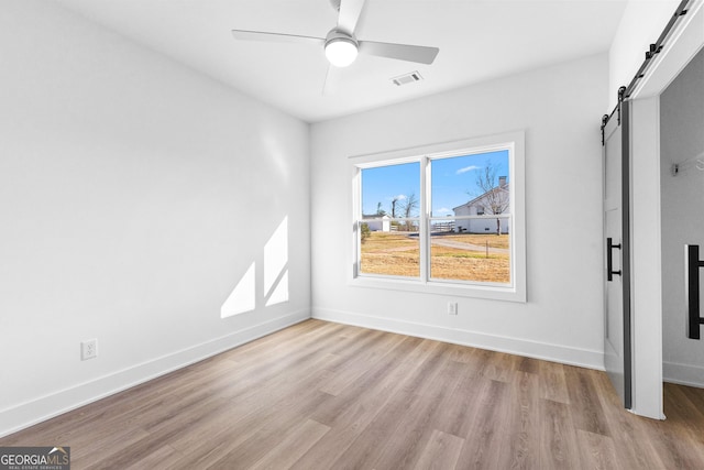 unfurnished bedroom with wood finished floors, visible vents, baseboards, and a barn door