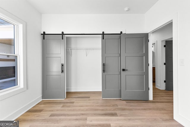 interior space featuring a closet, light wood-style flooring, baseboards, and a barn door