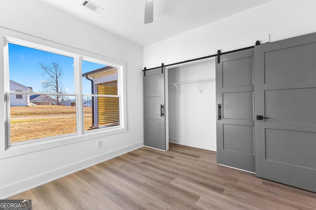 unfurnished bedroom featuring light wood finished floors, a barn door, visible vents, baseboards, and a closet