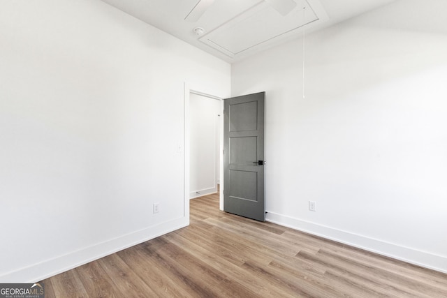 empty room with attic access, light wood-style flooring, and baseboards