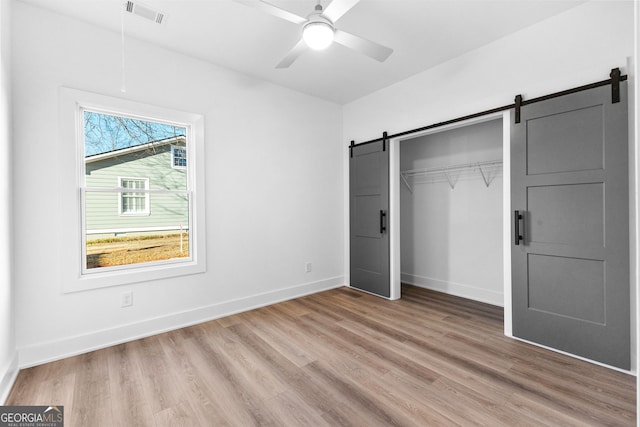 unfurnished bedroom featuring a closet, visible vents, a barn door, light wood-type flooring, and baseboards