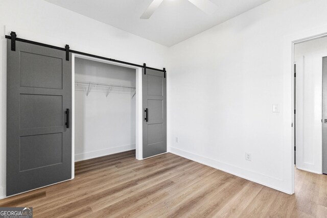 unfurnished bedroom featuring light wood-style floors, a barn door, baseboards, and a closet