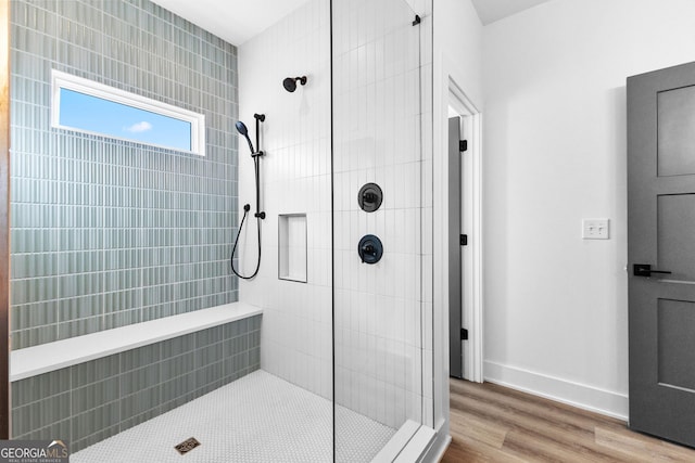 full bathroom featuring a tile shower, baseboards, and wood finished floors