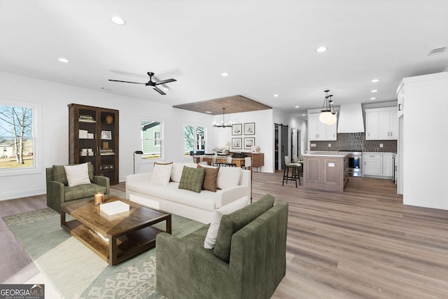 living room featuring recessed lighting, ceiling fan with notable chandelier, visible vents, baseboards, and light wood-style floors