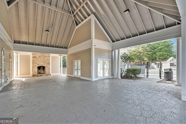 unfurnished living room with high vaulted ceiling, an outdoor stone fireplace, and french doors