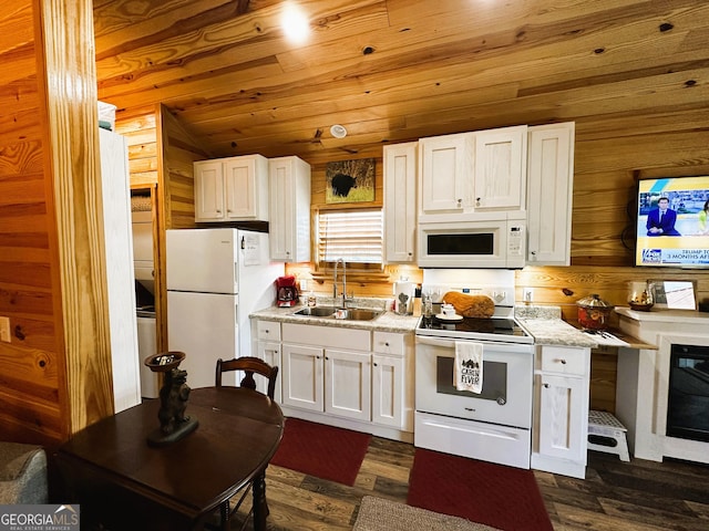 kitchen featuring white appliances, wooden walls, white cabinets, wood ceiling, and a sink