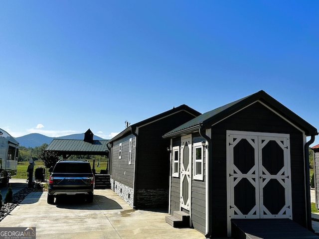 view of side of property featuring a mountain view, concrete driveway, a storage unit, and an outdoor structure