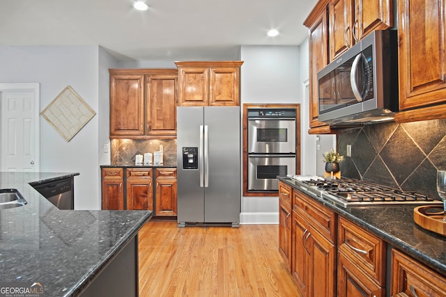 kitchen featuring dark stone countertops, appliances with stainless steel finishes, light wood-type flooring, and decorative backsplash