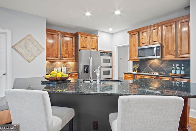 kitchen with appliances with stainless steel finishes, decorative backsplash, a large island with sink, wood-type flooring, and dark stone counters