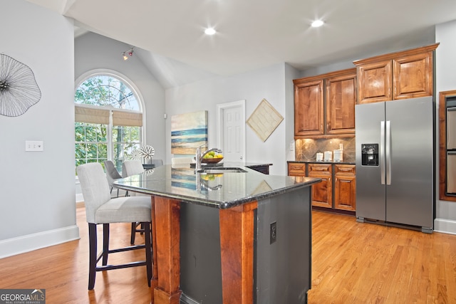 kitchen featuring vaulted ceiling, stainless steel fridge with ice dispenser, an island with sink, and light hardwood / wood-style flooring