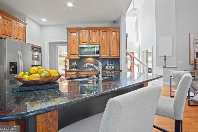 kitchen featuring hanging light fixtures, tasteful backsplash, stainless steel appliances, light wood-type flooring, and sink