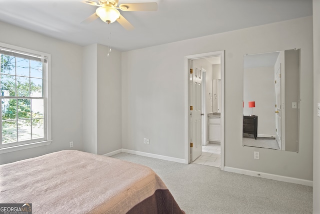 bedroom with ceiling fan, light colored carpet, and ensuite bath