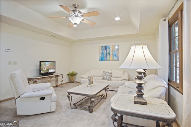 living room featuring light carpet, a tray ceiling, and ceiling fan