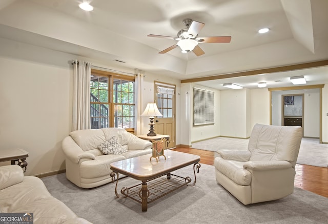 living room with light hardwood / wood-style flooring, a tray ceiling, and ceiling fan