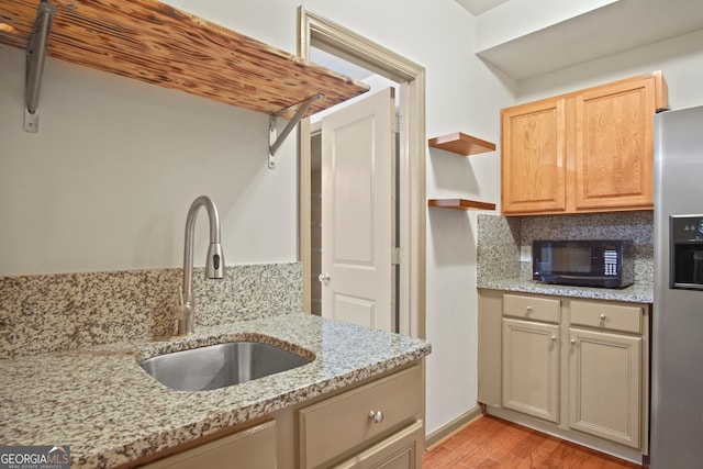 kitchen with stainless steel fridge, sink, light hardwood / wood-style flooring, and light stone countertops