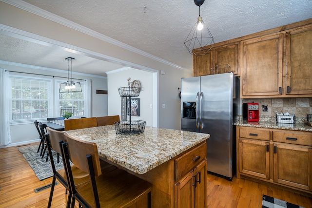 kitchen featuring hanging light fixtures, stainless steel refrigerator with ice dispenser, a center island, light wood-type flooring, and crown molding