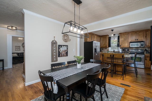 dining room featuring hardwood / wood-style flooring, crown molding, sink, and a textured ceiling