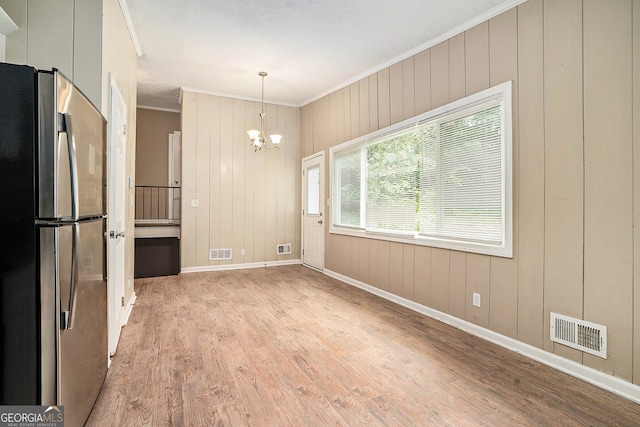 unfurnished dining area with wooden walls, ornamental molding, an inviting chandelier, and light hardwood / wood-style flooring