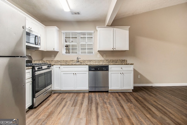 kitchen with white cabinetry, stainless steel appliances, wood-type flooring, dark stone counters, and sink