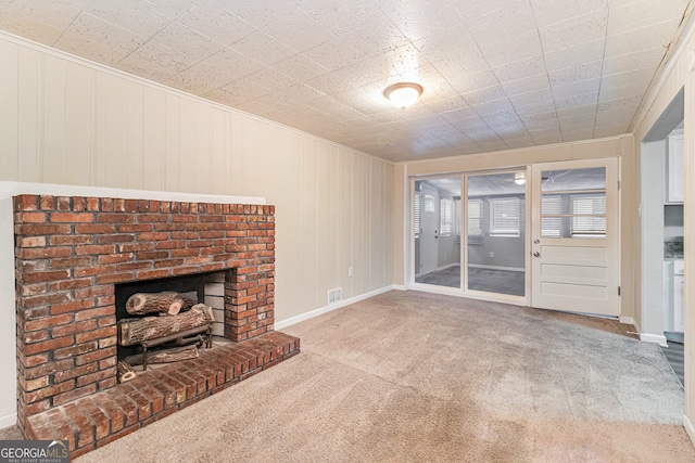 unfurnished living room with a fireplace, wooden walls, and light colored carpet