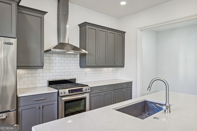 kitchen featuring wall chimney range hood, sink, stainless steel appliances, and backsplash