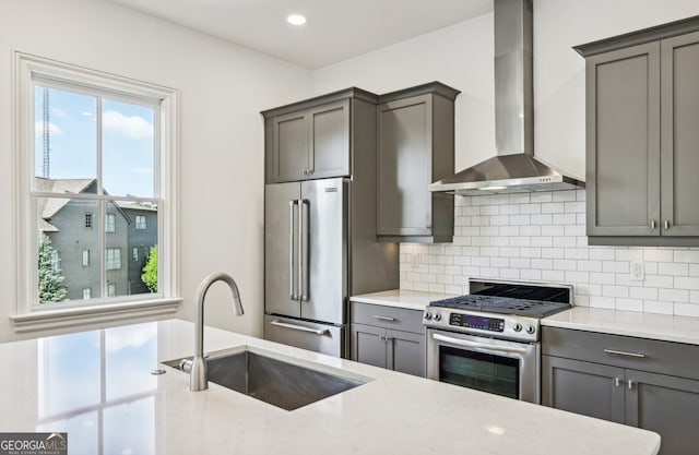 kitchen with sink, tasteful backsplash, gray cabinetry, wall chimney range hood, and appliances with stainless steel finishes