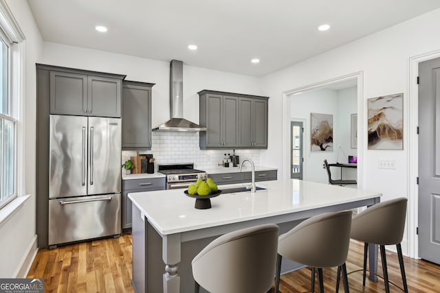 kitchen with light wood-type flooring, sink, wall chimney range hood, appliances with stainless steel finishes, and a kitchen breakfast bar