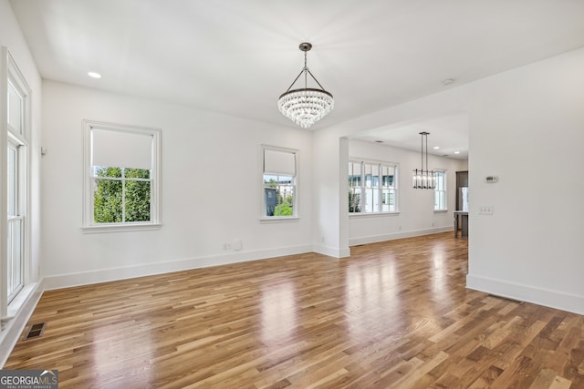 unfurnished living room with light wood-type flooring, plenty of natural light, and a chandelier