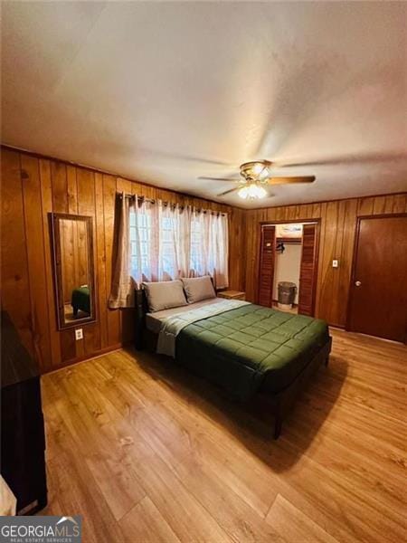 bedroom with light hardwood / wood-style floors, wood walls, and ceiling fan