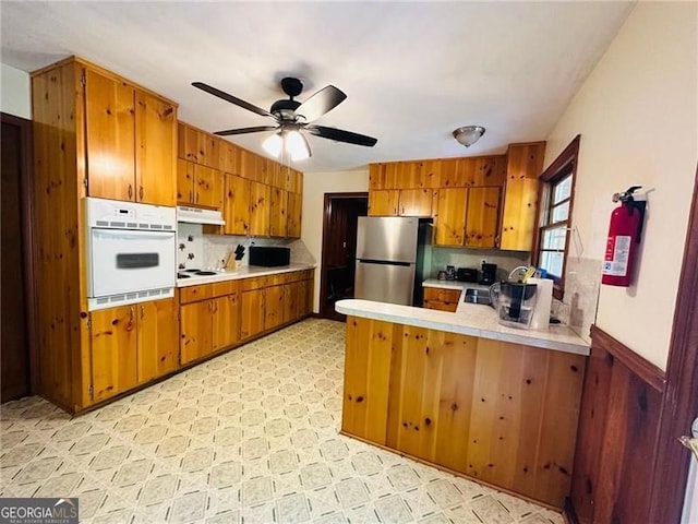 kitchen featuring ceiling fan, stainless steel fridge, kitchen peninsula, tasteful backsplash, and white oven