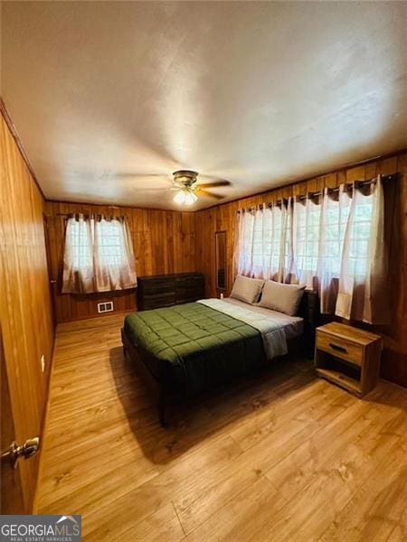 bedroom featuring ceiling fan, wooden walls, and light wood-type flooring