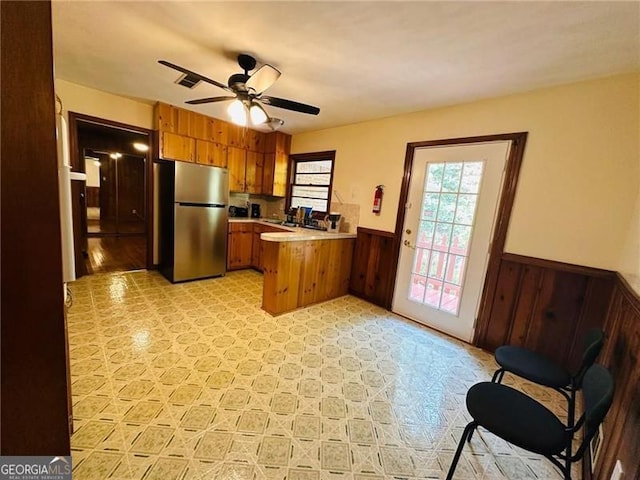 kitchen with ceiling fan, stainless steel refrigerator, wooden walls, and kitchen peninsula