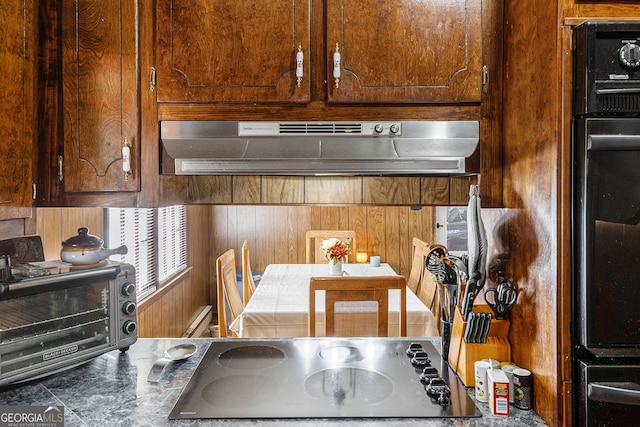 kitchen with wood walls, black appliances, and ventilation hood