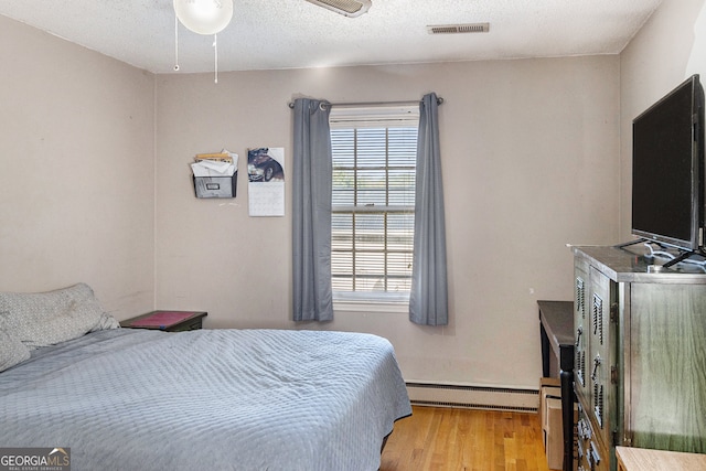 bedroom featuring baseboard heating, light wood-type flooring, a textured ceiling, and ceiling fan