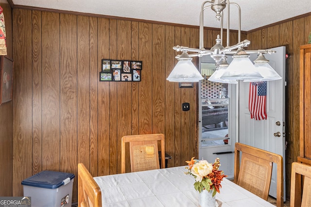 dining space featuring wooden walls, a textured ceiling, a notable chandelier, and crown molding