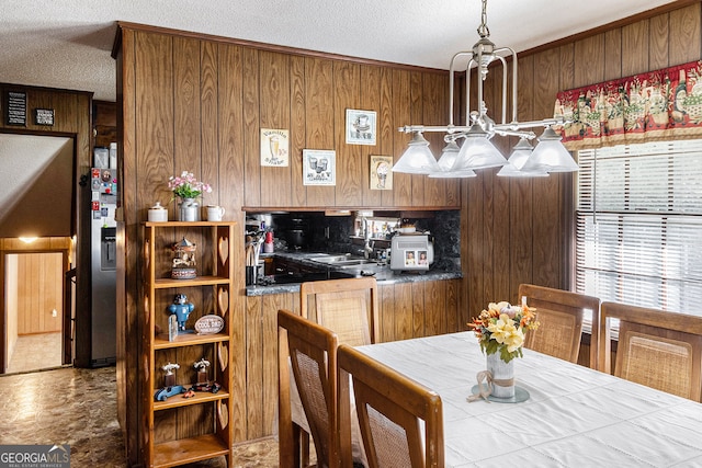 dining space featuring sink, wooden walls, a textured ceiling, and a notable chandelier