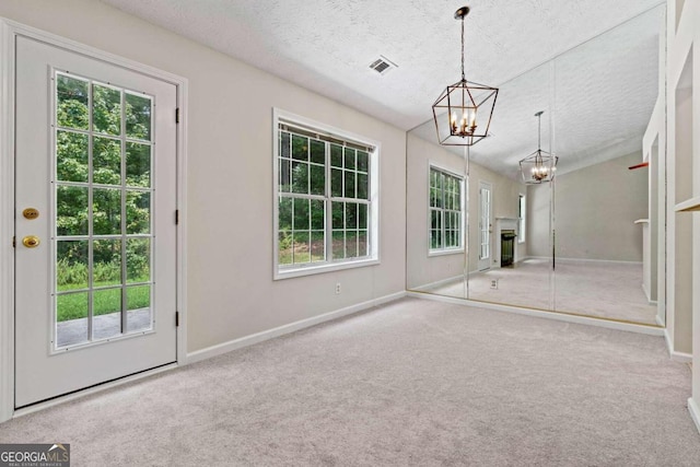 doorway to outside featuring a notable chandelier, a textured ceiling, carpet floors, and a healthy amount of sunlight