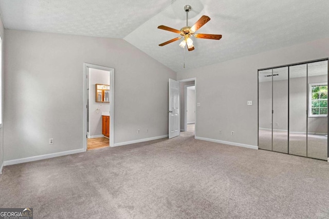 unfurnished bedroom with vaulted ceiling, connected bathroom, a closet, ceiling fan, and light carpet