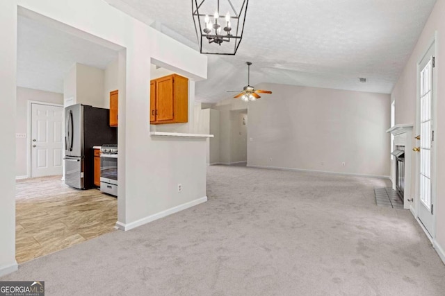 unfurnished living room featuring ceiling fan with notable chandelier, vaulted ceiling, and light colored carpet