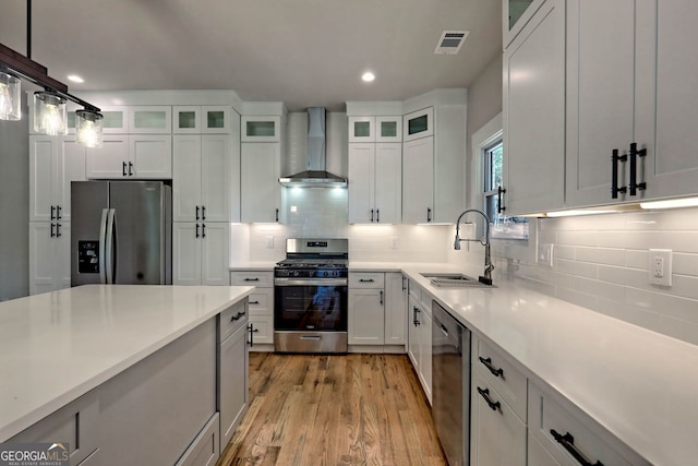 kitchen featuring wall chimney exhaust hood, white cabinetry, sink, and appliances with stainless steel finishes