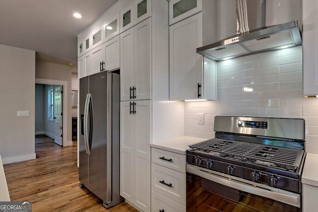 kitchen featuring backsplash, wall chimney exhaust hood, stainless steel appliances, light hardwood / wood-style flooring, and white cabinetry