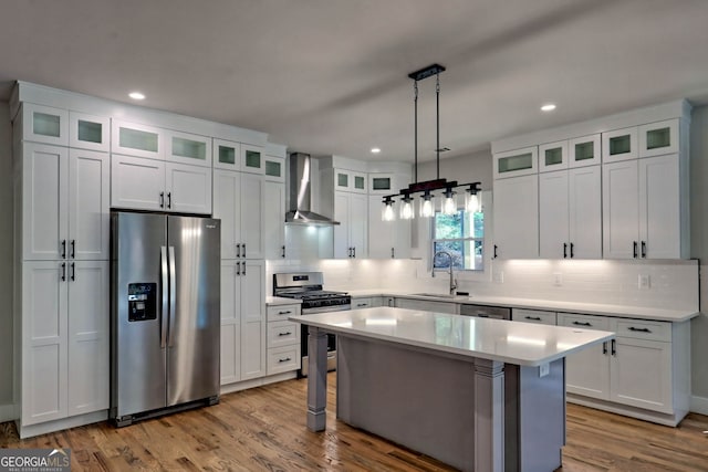 kitchen with white cabinetry, a kitchen island, wall chimney range hood, and appliances with stainless steel finishes