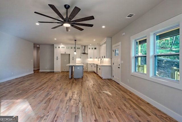 kitchen with wall chimney exhaust hood, ceiling fan, white cabinets, a center island, and light hardwood / wood-style floors