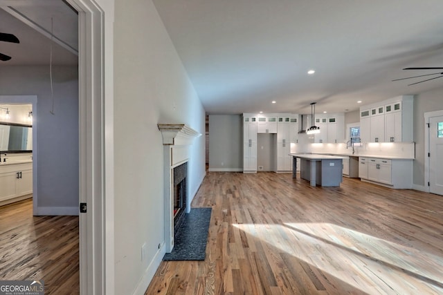 kitchen featuring pendant lighting, light hardwood / wood-style flooring, ceiling fan, wall chimney exhaust hood, and white cabinetry